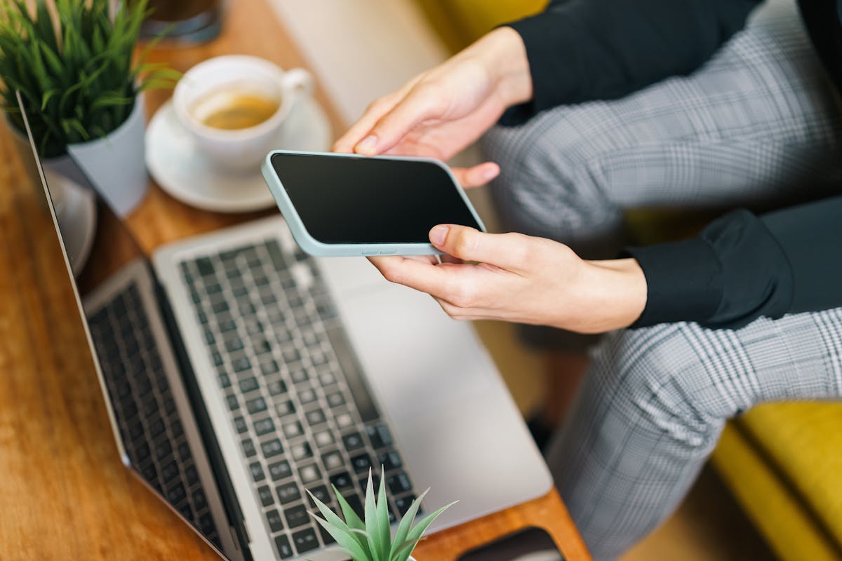 Persoon gebruikt smartphone en laptop aan een bureau